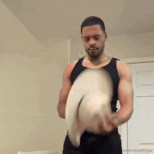 a man in a tank top is holding a cowboy hat in his hands .