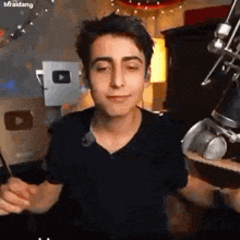 a young man in a black shirt is standing in front of a microphone in a room .