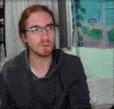 a man wearing glasses and a grey sweater is sitting in front of a window