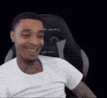 a man in a white shirt is sitting in a gaming chair and smiling .