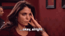 a woman is holding her head and saying " okay alright "