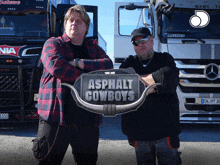 two men standing in front of a truck with a sign that says asphalt cowboys on it