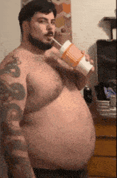 a shirtless man with a beard is drinking through a straw from a cup .