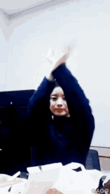 a woman is sitting at a table with her arms in the air