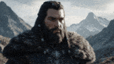 a man with long hair and a beard is standing in front of mountains and the word veo is on the bottom