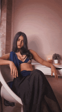 a woman in a blue top and black skirt is sitting in a white chair