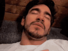 a man with a beard is sleeping on a bed with his eyes closed