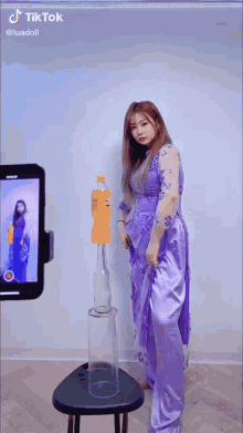 a woman in a purple dress is standing next to a bottle of orange soda and a glass