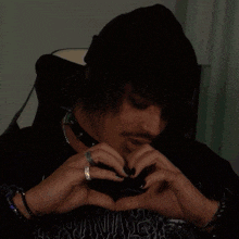 a man wearing a black hat and a choker is making a heart shape