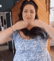 a woman in a blue dress is making a heart shape with her hands .