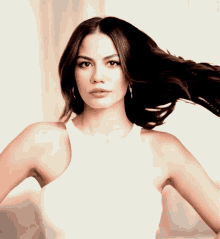 a woman in a white tank top with her hair blowing