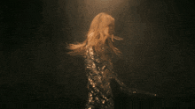 a woman in a sequined dress has her arms outstretched in a dark room