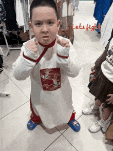 a little boy in a karate outfit stands in front of a sign that says lets fight