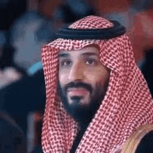 a man with a beard is wearing a red and white checkered keffiyeh .
