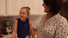 a little girl is sitting next to a woman in a kitchen and smiling .