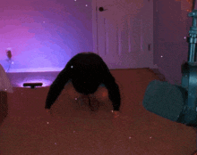 a person is doing a handstand in a room with a purple light behind them .