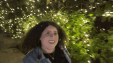 a woman with curly hair is smiling in front of a christmas tree