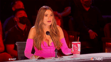 a woman in a pink dress is sitting in front of a microphone holding a cup that says bud light