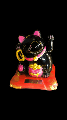 a statue of a black cat with a pink collar and a yellow bag that says ' wealth ' on it