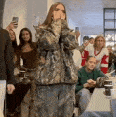 a woman in a camo jacket is covering her face while standing in front of a crowd of people .