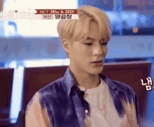 a young man with blonde hair is wearing a purple tie dye shirt .