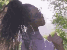 a woman wearing sunglasses and a ponytail is standing in front of trees .