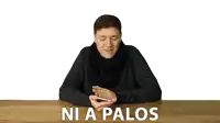 a man is sitting at a table holding a cell phone and the words ni a palos are above him