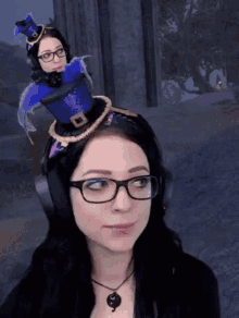 a woman wearing glasses and a purple top hat has a doll on her head