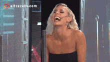 a woman is laughing in front of a screen with eltrecetv.com written on it
