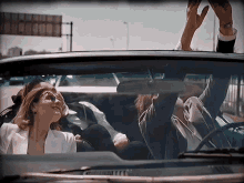 a man and a woman in a car with their arms in the air