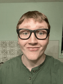 a man wearing glasses and a green shirt looks at the camera