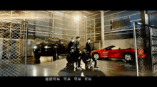 a group of people are standing in front of a red car in a garage