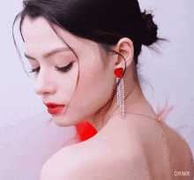 a close up of a woman 's face wearing a bun and red earrings