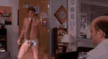 a shirtless man in underwear is standing in a living room next to a man in a suit and tie .