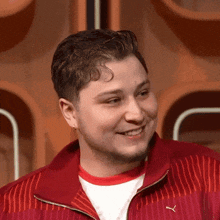 a young man wearing a red puma jacket smiles