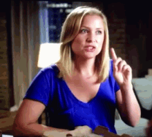 a woman in a blue shirt is making a funny face and pointing up .