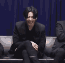 a man in a suit is sitting next to another man in a hat and laughing .