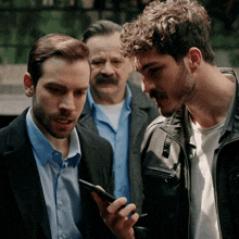 a man in a black jacket looks at a cell phone