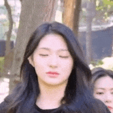a close up of a woman with her eyes closed standing in front of a tree .