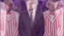 a man in a suit and tie is standing in front of two men in pink and white striped jackets .