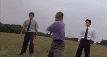 a man in a purple shirt stands in a field with two other men