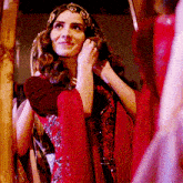 a woman in a red dress is smiling and looking at herself in the mirror