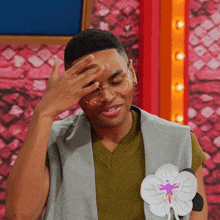 a man wearing glasses and a vest with a flower on it covering his face