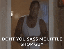 a man in a white tank top is standing in a doorway holding a hair dryer and talking to someone .