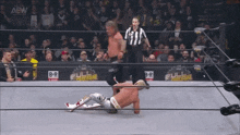 a wrestler is laying on the ground in a wrestling ring while a referee stands behind him .