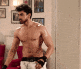 a shirtless man with a beard stands in a room with pictures on the wall