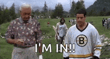 a man in a boston bruins jersey is standing on a golf course next to another man .