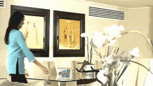 a woman in a blue shirt is arranging a table in front of two framed pictures