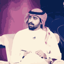 a man with a beard wearing a head scarf and a white shirt is sitting in a chair