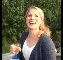 a woman in a blue cardigan is holding a glass of wine and smiling .